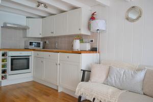 une cuisine avec des armoires blanches et un canapé dans une pièce dans l'établissement Sailmaker's Cottage, à Shaldon