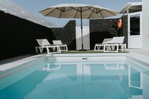 a pool with two chairs and an umbrella at Villa Lanzarote Zen in Playa Blanca