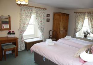 a bedroom with two beds and a desk and windows at Corner House in Grinton