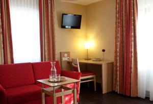 Habitación de hotel con sofá rojo y escritorio. en Hotel Rosenhof Garni en Pegnitz