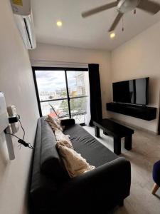 ein Wohnzimmer mit einem schwarzen Sofa und einem TV in der Unterkunft Acogedor Fast WIFI 5ta Avenida in Playa del Carmen