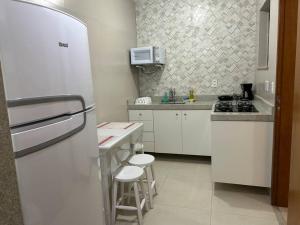 a white kitchen with a refrigerator and stools in it at Novíssimo apt 1 quarto Centro frente à Prefeitura in Nova Friburgo