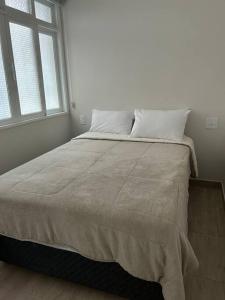 a bed in a white room with two windows at Novíssimo apt 1 quarto Centro frente à Prefeitura in Nova Friburgo