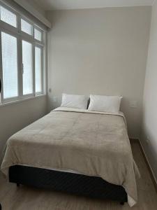 a bed in a white room with two windows at Novíssimo apt 1 quarto Centro frente à Prefeitura in Nova Friburgo