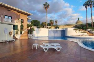 a swimming pool with two white benches and a house at Club Paraiso in Adeje