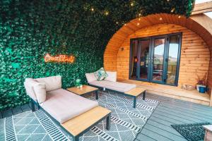 d'une terrasse avec deux canapés et des tables en face d'un mur vert. dans l'établissement Bonnie Brae - (Luxury Pod), à Portpatrick