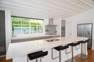 a white kitchen with a large island with bar stools at Tahapuke by Amazing Accom in Russell