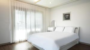 ein weißes Schlafzimmer mit einem weißen Bett und einem Fenster in der Unterkunft Ganghwa Hanabi Pension in Incheon