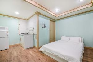 a bedroom with a white bed and a kitchen at Sokcho Dderak Pension in Sokcho