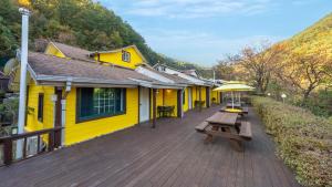 a yellow building with a wooden deck with benches at Gangneung Sinami68 Pension in Gangneung