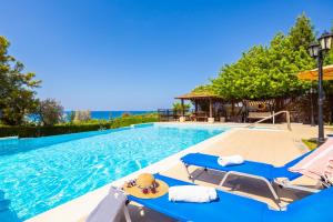 a swimming pool with two blue lounge chairs and the ocean at Villa Ariadne in Argaka