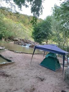 a picnic table with a blue canopy next to a river at Balneário Rio Agua Viva - Área de Camping in Areia