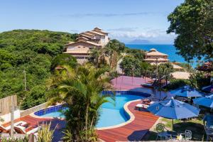 a resort swimming pool with blue umbrellas and the ocean at La Proeza Pousada in Búzios