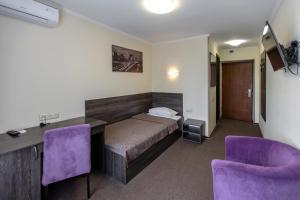 a bedroom with a bed and a desk and purple chairs at Dnepropetrovsk Hotel in Dnipro