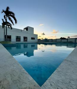 a swimming pool in front of a building with a palm tree at Apartamento na praia, 2 quartos e área de lazer in Cabedelo
