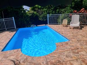 a blue swimming pool with two chairs and a fence at Gîte L'adérobade in Le Gosier +3 photos