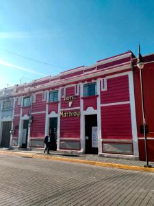a red and white building with a man walking past it at Hotel Marmoy in Cholula