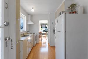 a kitchen with white cabinets and a white refrigerator at Downtown Cosy Cottage in Mount Maunganui +12 photos