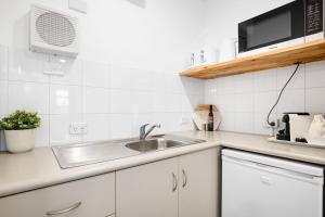 a white kitchen with a sink and a microwave at Bayscape Studio Glenelg in Glenelg