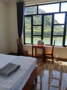 a bedroom with a bed and a table and windows at Duong Riverside Homestay in Phong Nha