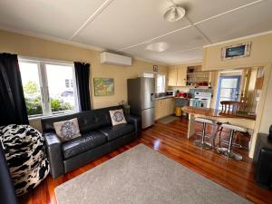 a living room with a black couch and a kitchen at Relaxing Raglan & the Boat House in Raglan