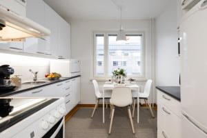 a kitchen with white cabinets and a table with white chairs at Santa's Luxury City Apartment 3 in Rovaniemi