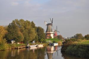 a mill and boats on a river with a windmill at Ferienhaus Strandläufer in Krummhörn