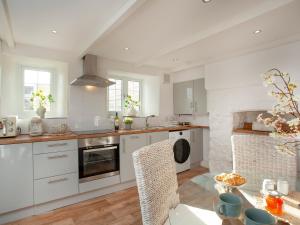 a kitchen with white cabinets and a table with chairs at Harlequin Cottage in St Austell +26 photos