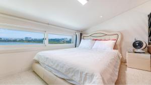 a white bedroom with a large bed and a window at Gangneung Olraeendaol Spa Pension in Gangneung