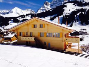 a yellow house in the snow with mountains in the background at Apartment Butterfly by Interhome in Adelboden