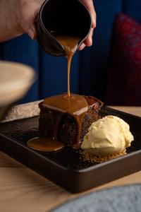 iemand die koffiesaus over een stuk taart met ijs druppelt bij Penrhos Park in Aberystwyth