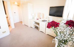 a room with a desk with flowers and a tv at Haddon House Hotel in Bridport