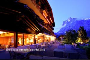 a building with tables and chairs and a mountain at Hotel Kirchbühl Superior in Grindelwald