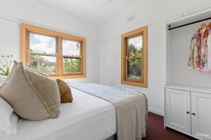 a white bedroom with a bed and two windows at The Waratah House close to town center in Katoomba