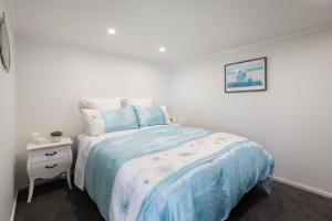 a white bedroom with a bed and a night stand at Two Palms - Waihi Beach Holiday Apartment in Mangonui