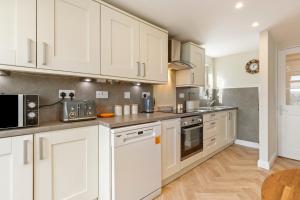 a kitchen with white cabinets and stainless steel appliances at Gorse Cottage - Sea Views Village Centre in Penally