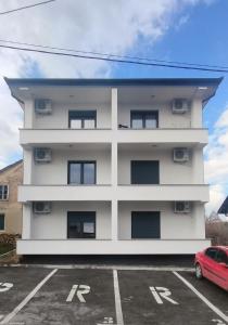 a white building with a car parked in a parking lot at Bella Vacanza Apartment in Banja Luka