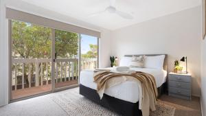 a white bedroom with a bed and a large window at Thistledoo in Callala Beach