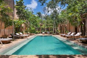 a swimming pool with lounge chairs and trees in front of a building at 3BR Home in Gated Community with Private Rooftop Plunge Pool, Grill & Shared Pool in Tulum
