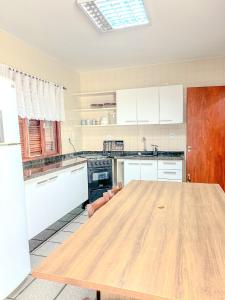 una gran mesa de madera en una cocina con armarios blancos en Casa Maré de Bombas - em Pousada Maré de Bombas, en Bombinhas
