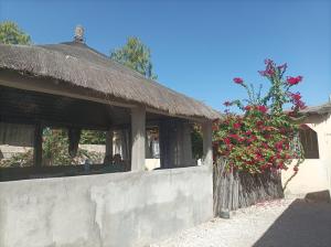 un edificio con techo de paja y un arbusto con flores rosas en Keur Karim, en Niodior