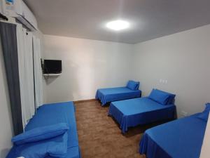 a room with two blue beds and a tv at Pousada DONA DUTRA in Lençóis Paulista