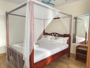 ein Schlafzimmer mit einem Himmelbett mit weißer Bettwäsche und Kissen in der Unterkunft Maanet Gardens Hotel in Kutu