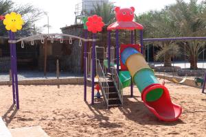 a playground with a slide in the sand at ghroob farmhouse villa in Al Ḩamrānīyah