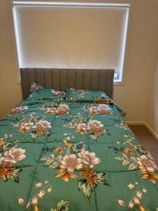 a bed with a green comforter with flowers on it at The Blissful Abode in Truganina