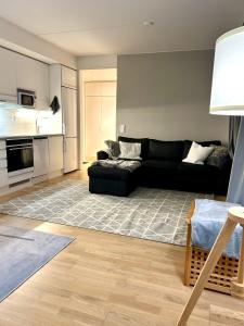 a living room with a black couch and a kitchen at Moderni viihtyisä kaksio Jyväskylässä ilmaisella pysäköintipaikalla in Jyväskylä