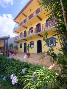 a yellow building with a courtyard with purple flowers at Pousada Luz do Sol in Carrancas