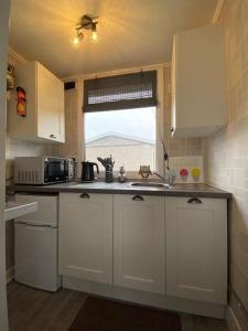 a kitchen with white cabinets and a sink and a window at Sandy Paws in Trusthorpe +12 photos