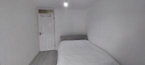 a small white room with a bed and a door at London Travellers Room - Romford, Hornchurch, Gidea Park to Heathrow via Elizabeth line in Harold Wood
