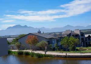 a building by the water with mountains in the background at Lakeside Apartment in Oubaai Golf Estate in George